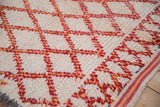 Textured pile of vintage Moroccan rug, ivory with red and tangerine lattice, intact striped selvage.