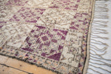 Moroccan carpet fringe with visible side selvage next to violet, ivory, and apricot patterns.