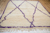Plush ivory pile and fringe of a vintage Moroccan carpet with violet diagonal lines.