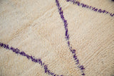 Close-up of shaggy ivory pile with geometric violet purple lattice vines on Moroccan rug.
