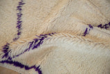 Thick, even ivory pile with strong violet lines on a Moroccan carpet.