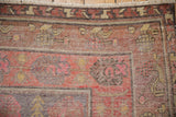 Distressed Khotan rug corner, highlighting worn texture, exposed foundation, and faded purple and red motifs.