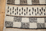 Vintage Moroccan carpet's textured pile, side selvage, and checkered horizontal patterns in ivory and black.