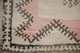 Worn Moroccan rug pile revealing the foundation, with dark brown starburst patterns over ivory and pale rose.