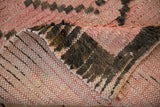 Folded vintage Moroccan rug, showing pink wool pile with charcoal diamonds and cotton flatweave reverse.