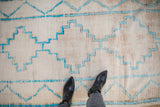 Cream vintage Moroccan rug with turquoise stepped patterns, visible foundation wear, and black boots.