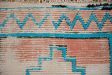Detail of vintage Moroccan runner showing textured pile, turquoise chevron, blush pink, and wear to foundation.