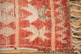 Corner detail of a vintage Moroccan rug showing dusty red pile, intact selvage, and braided fringe.