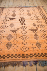 Textured pile of pale tangerine vintage Moroccan rug with brown bird and diamond motifs.