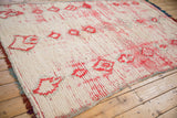 Textured ivory pile of a vintage Moroccan carpet with red geometric motifs revealing the foundation.