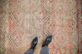 Black boots on a vintage Moroccan rug, showing geometric trellis and floral motifs in blush and beige.