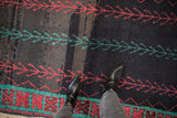 Abrashed charcoal ground and hand-knotted pile of a Moroccan rug with red and emerald green vine patterns.
