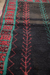 Angled view of the hand-knotted texture of a Moroccan rug with red and turquoise vine motifs.