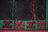 Plush charcoal pile with red and green vine motifs and a geometric turquoise border.