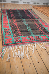 Low angle view of a vintage Moroccan rug, showing its white fringe and abrashed charcoal pile.