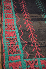 Close-up of a vintage Moroccan rug's turquoise border with red crab-style motifs and charcoal field.