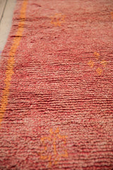 Textured pile of vintage Moroccan runner, featuring faded raspberry red and orange floral accents.