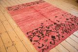 Angled view of a Moroccan carpet's raspberry red textured pile and abstract brown motifs.