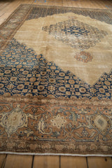 Low angle on a distressed Tabriz carpet highlights the intricate navy Herati spandrel and worn camel field.