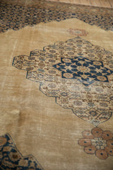 Angled view of a vintage Tabriz rug's distressed pile and scalloped camel and navy medallion.