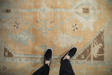 Distressed vintage Oushak carpet featuring abrashed sand field with light blue and brown patterns.