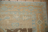 Distressed Oushak rug corner showing knot heads, soft sand, and blue cloudband motifs.