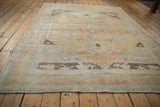 Corner view of distressed Oushak rug with abrashed sand field and pale blue stylized motifs.
