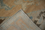 Lifted corner of vintage Oushak rug, revealing hand knotted foundation and sand, gold, blue distressed pile.