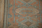 Distressed Hamadan rug detail: cantaloupe and blue floral medallions, narrow vine border, worn pile.