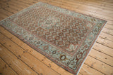 Antique Malayer rug shown at an angle, displaying its rust red field, hexagonal medallion, and slate blue border.