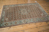 Angled view of a distressed antique Malayer rug with a rust field and complex slate blue border.