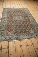 Angled view of an antique Malayer rug's henna blossom field and slate blue turtle border.