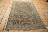 Distressed Persian Hamadan rug with coffee brown and turquoise bird motifs, viewed from an angle.
