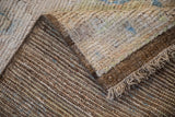 Distressed Afghani Oushak carpet: ivory textured pile, dark woven foundation, selvage, and fringe.