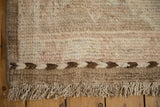 Distressed Afghani Oushak carpet corner, showcasing braided ivory and brown selvage with natural fringe.