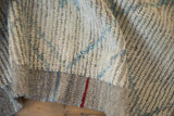 Distressed Afghani Moroccan carpet close-up, featuring ivory pile, dark wefting, and blue/red selvage lines.