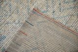 Distressed Afghani Moroccan hand-knotted carpet pile in ivory and blue, revealing the woven gray foundation.