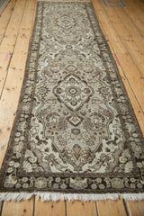Angled, full-length view of a distressed Persian runner with repeating floral medallions in brown and silver.