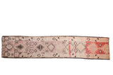 A vintage distressed Moroccan runner with asymmetric diamond medallions in mauve, charcoal, and faded cherry red.