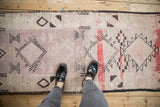 A person's view of a distressed Moroccan runner's faded mauve, red, and charcoal geometric patterns.