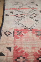 Close-up of the distressed knot heads and faded red motifs on a hand-knotted Moroccan runner.