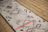 Angled view of a distressed Moroccan runner with faded mauve tones and charcoal diamond motifs.