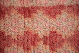 Thick shaggy pile of a distressed Moroccan rug in faded reds, pinks, and ivory.