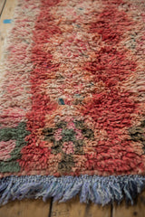 Distressed Moroccan rug's shaggy red, pink, and ivory pile with fading tips and blue fringe.