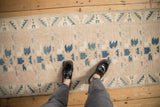 Looking down at the worn, low-pile texture of a mauve and blue Oushak runner.
