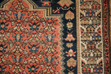 Intricate geometric border motifs of an antique Malayer rug in navy blue, beige, and tomato red.