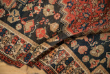 Hand-knotted texture of a folded antique Malayer rug with navy, red, and sand floral motifs.