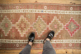 Distressed Kurd runner with stepped geometric medallions, germinating vine border, and faded cochineal tones.