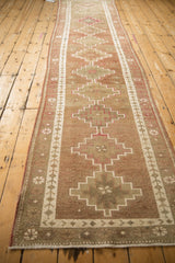 Distressed Kurd runner detail: stepped medallions, vine border, and dusty cochineal red.
