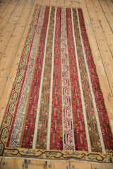 An angled, full-length view of a vintage Anatolian runner with parallel geometric stripes in red and green.